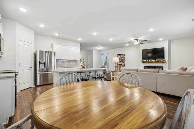 dining space featuring ceiling fan, a large fireplace, and dark wood-type flooring