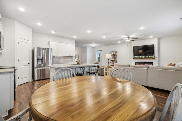 dining space with ceiling fan, dark hardwood / wood-style flooring, and a fireplace