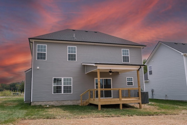 back house at dusk with a lawn, ceiling fan, cooling unit, and a deck