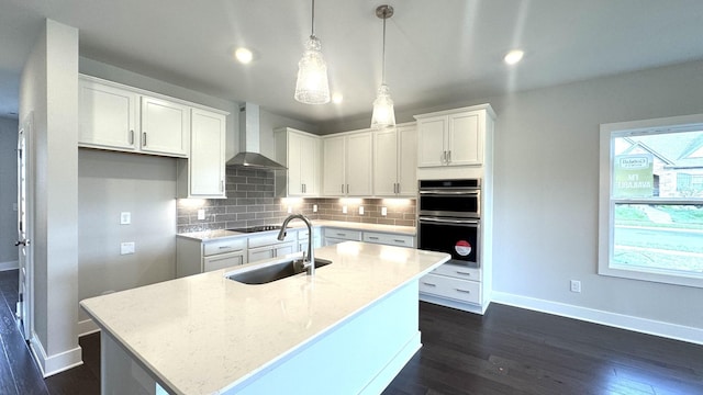 kitchen featuring wall chimney exhaust hood, stainless steel double oven, sink, pendant lighting, and white cabinetry