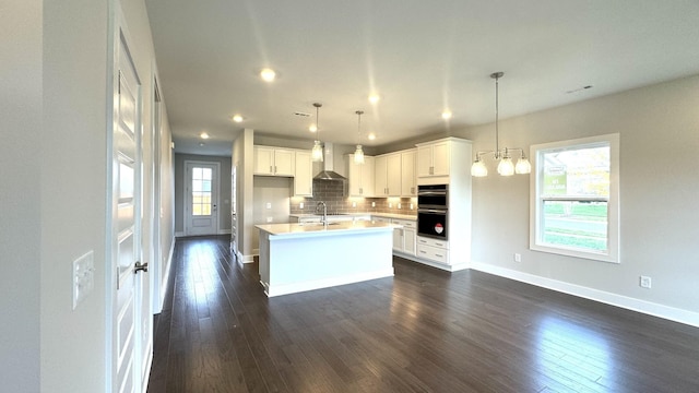 kitchen with backsplash, sink, pendant lighting, white cabinetry, and an island with sink