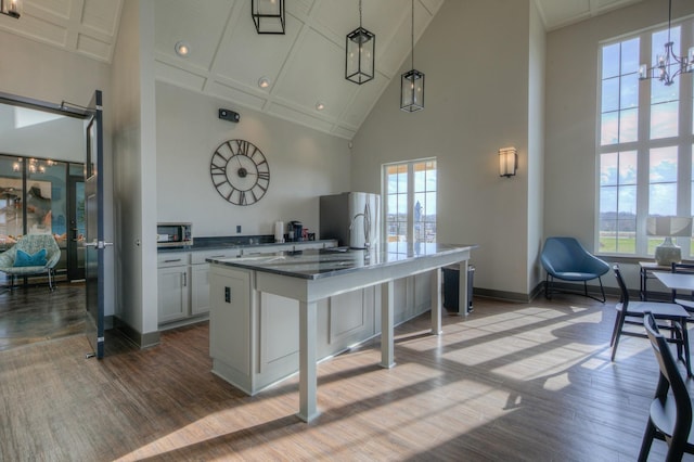 kitchen featuring white cabinetry, a towering ceiling, an island with sink, and hanging light fixtures