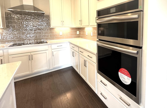 kitchen featuring black electric stovetop, tasteful backsplash, stainless steel double oven, wall chimney range hood, and dark hardwood / wood-style floors