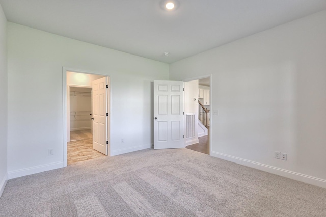 unfurnished bedroom with a walk in closet, light colored carpet, and a closet