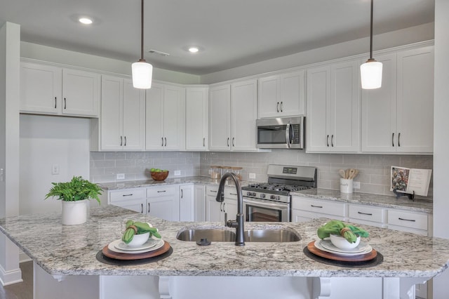 kitchen with white cabinetry, stainless steel appliances, hanging light fixtures, and an island with sink