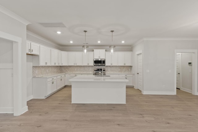 kitchen with pendant lighting, stainless steel appliances, a center island with sink, and white cabinets