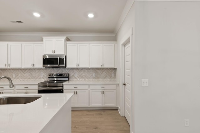 kitchen featuring sink, white cabinetry, light hardwood / wood-style flooring, ornamental molding, and appliances with stainless steel finishes