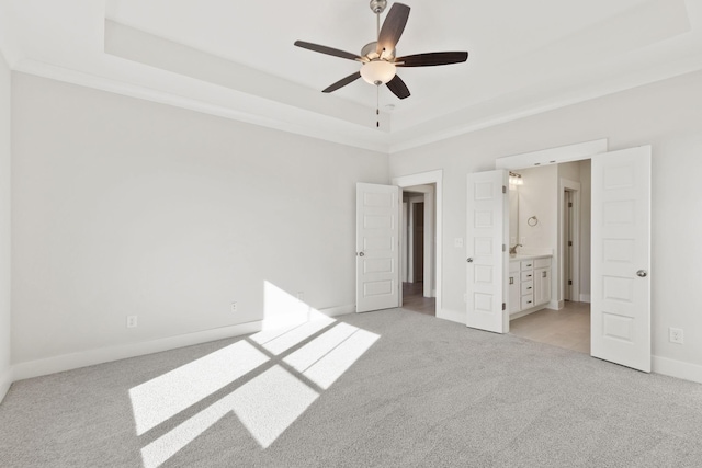 unfurnished bedroom with ceiling fan, light colored carpet, ensuite bath, and a tray ceiling