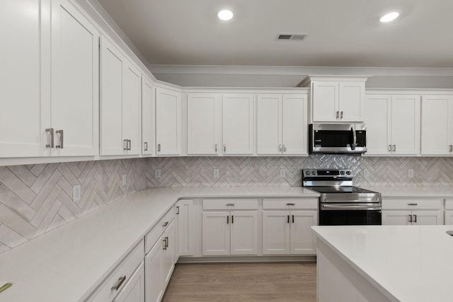 kitchen featuring light wood-type flooring, ornamental molding, white cabinets, and appliances with stainless steel finishes