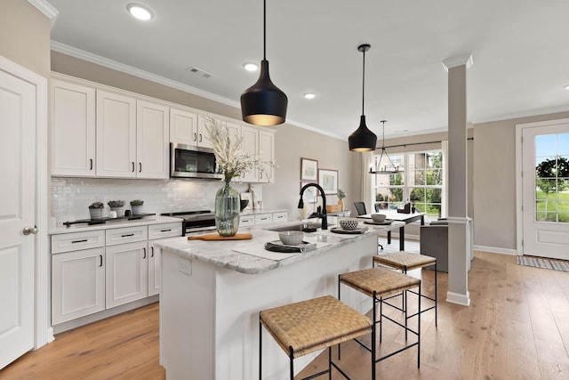 kitchen with stainless steel appliances, white cabinetry, a kitchen island with sink, and decorative light fixtures