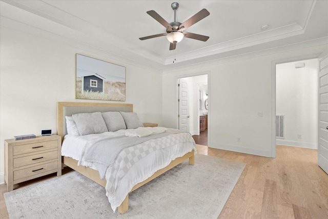 bedroom with ensuite bathroom, light wood-type flooring, ceiling fan, a tray ceiling, and crown molding