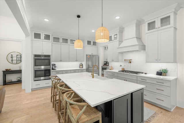 kitchen with white cabinetry, appliances with stainless steel finishes, a kitchen island with sink, and custom exhaust hood