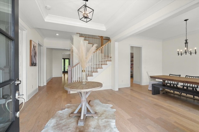 entryway with a raised ceiling, an inviting chandelier, crown molding, and light hardwood / wood-style floors