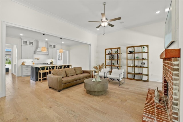 living room featuring ceiling fan, crown molding, a fireplace, and light hardwood / wood-style flooring