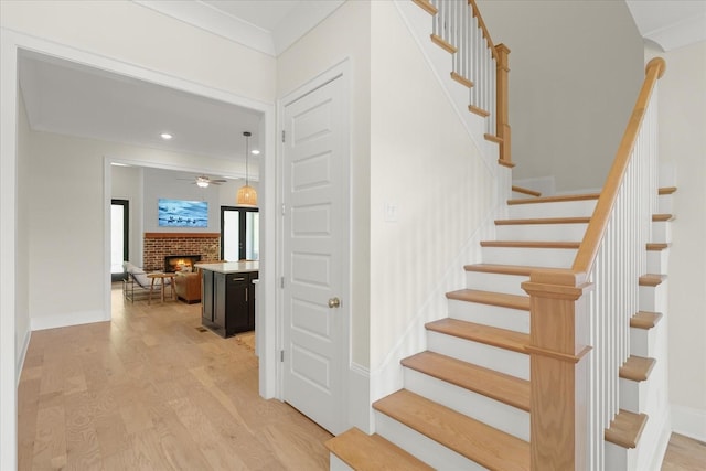 stairway with hardwood / wood-style flooring, ornamental molding, and a fireplace