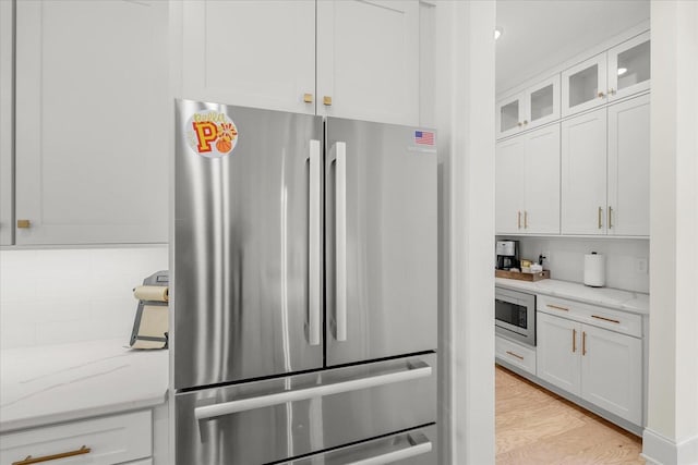 kitchen with backsplash, light hardwood / wood-style floors, light stone countertops, appliances with stainless steel finishes, and white cabinets