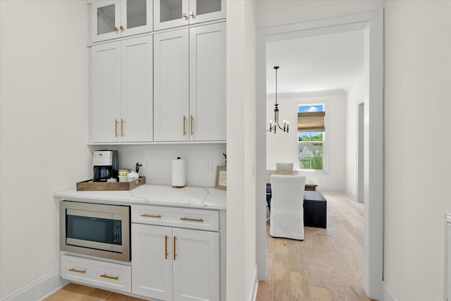 kitchen with white cabinetry, stainless steel microwave, backsplash, pendant lighting, and light hardwood / wood-style flooring