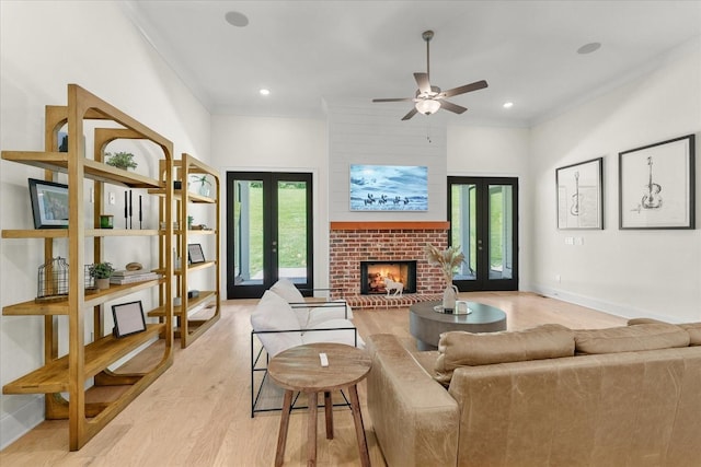 living room with a brick fireplace, french doors, light wood-type flooring, ceiling fan, and crown molding