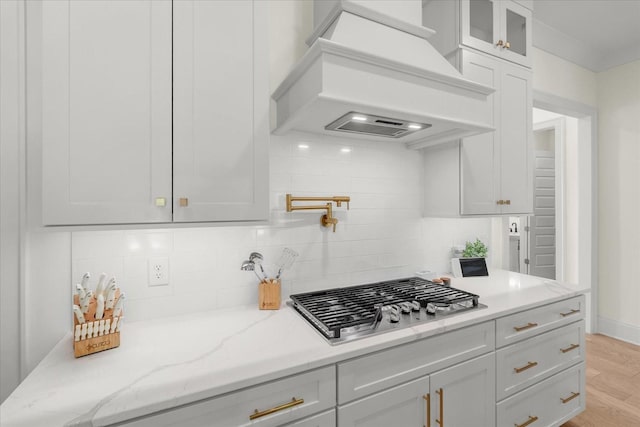 kitchen featuring stainless steel gas stovetop, decorative backsplash, custom exhaust hood, and light hardwood / wood-style flooring