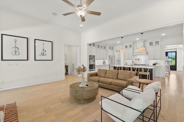 living room with ceiling fan, sink, crown molding, and light hardwood / wood-style flooring