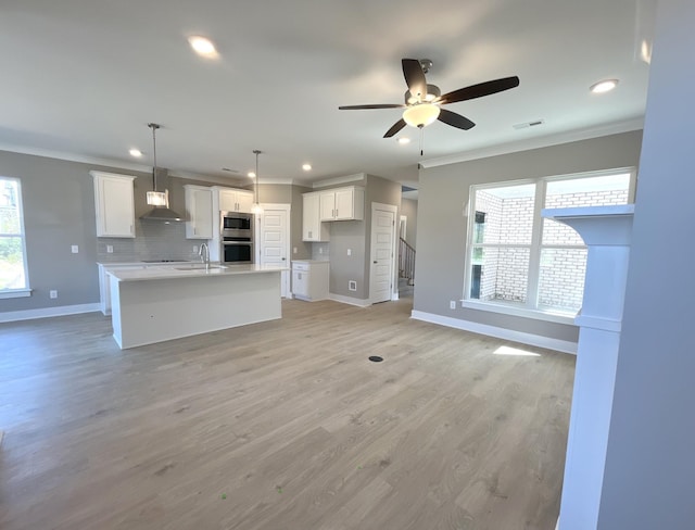 kitchen with backsplash, white cabinets, a center island with sink, light wood-type flooring, and decorative light fixtures