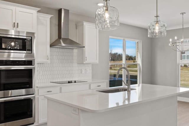 kitchen featuring sink, appliances with stainless steel finishes, white cabinets, a center island with sink, and wall chimney exhaust hood