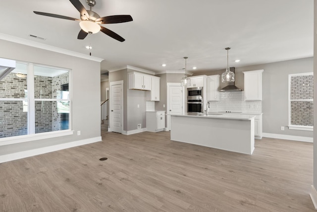 kitchen featuring stainless steel microwave, hanging light fixtures, wall chimney range hood, and white cabinets