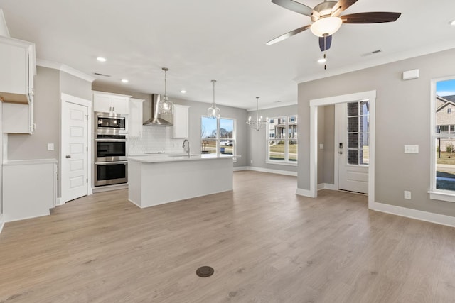 kitchen with pendant lighting, wall chimney range hood, stainless steel appliances, and an island with sink