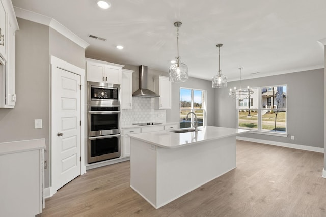 kitchen with sink, appliances with stainless steel finishes, an island with sink, white cabinets, and wall chimney exhaust hood