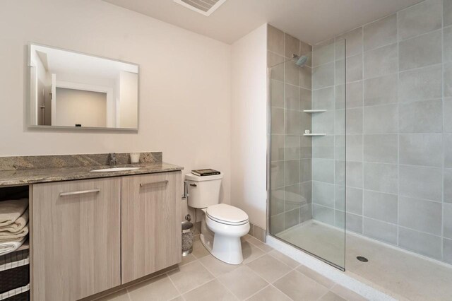 bathroom featuring vanity, a tile shower, toilet, and tile patterned floors