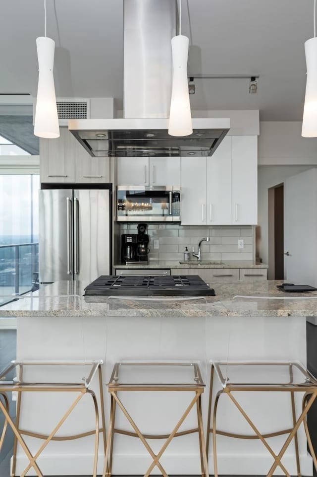 kitchen with appliances with stainless steel finishes, a breakfast bar, island exhaust hood, white cabinetry, and pendant lighting