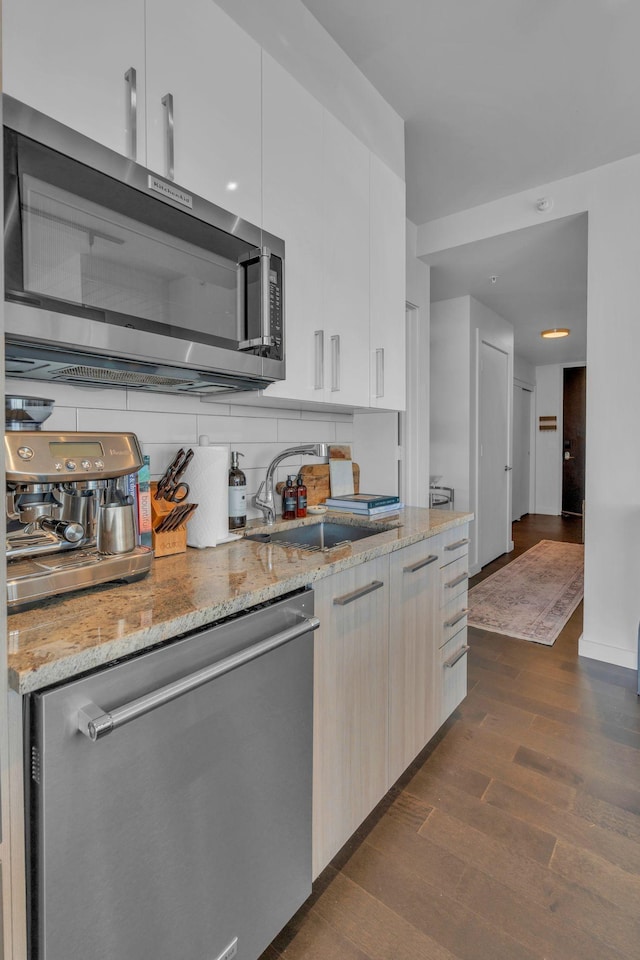 kitchen with sink, stainless steel appliances, light stone countertops, and dark wood-type flooring