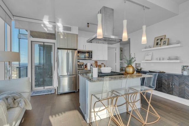 kitchen with appliances with stainless steel finishes, a breakfast bar area, island range hood, decorative light fixtures, and dark stone countertops