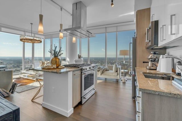 kitchen featuring hanging light fixtures, island range hood, light stone counters, and appliances with stainless steel finishes