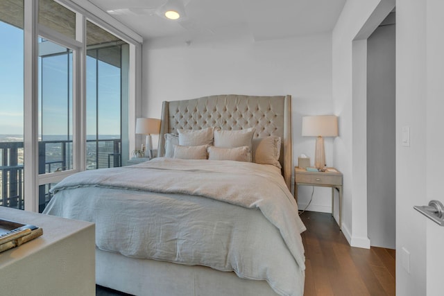 bedroom with a wall of windows and dark wood-type flooring