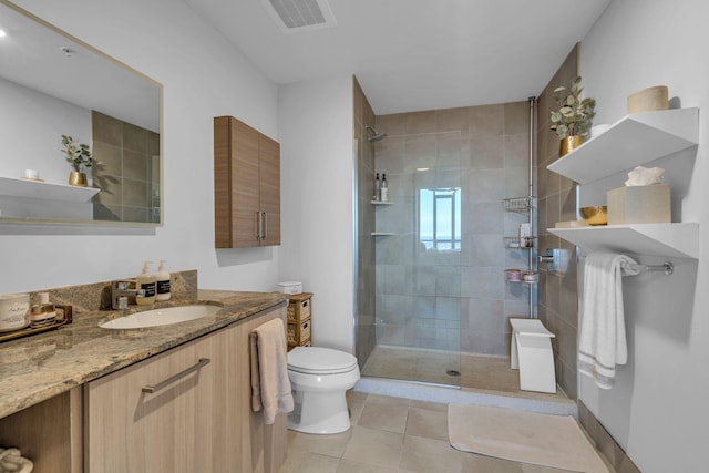 bathroom featuring a tile shower, vanity, tile patterned flooring, and toilet