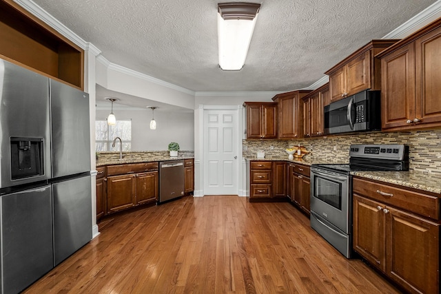 kitchen with light stone counters, crown molding, appliances with stainless steel finishes, hardwood / wood-style flooring, and decorative backsplash