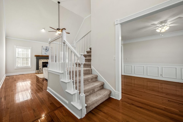 stairway featuring crown molding, ceiling fan, wood-type flooring, and a stone fireplace