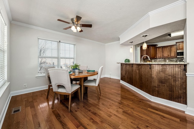 dining space with sink, crown molding, dark wood-type flooring, ceiling fan, and a textured ceiling