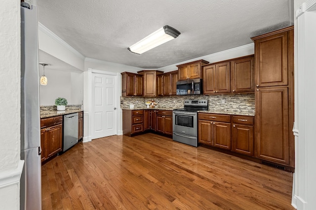 kitchen with dark wood-type flooring, crown molding, appliances with stainless steel finishes, light stone countertops, and backsplash