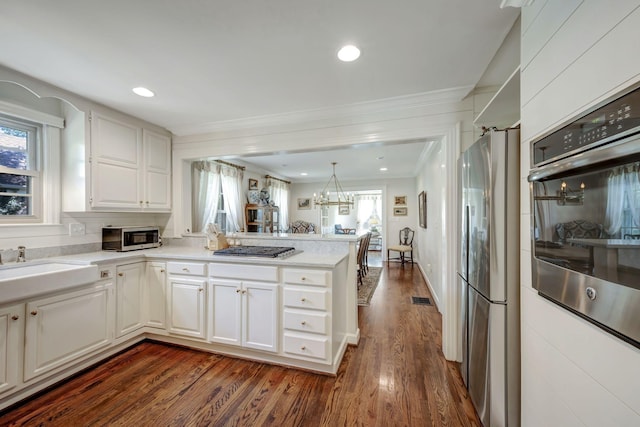 kitchen with sink, kitchen peninsula, appliances with stainless steel finishes, decorative light fixtures, and white cabinetry