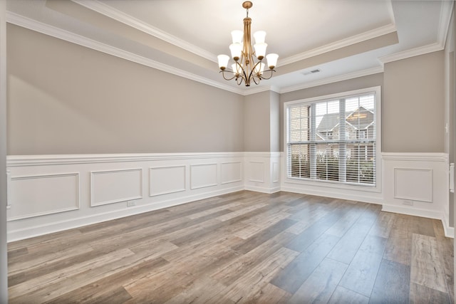 empty room with a raised ceiling, wood-type flooring, ornamental molding, and an inviting chandelier