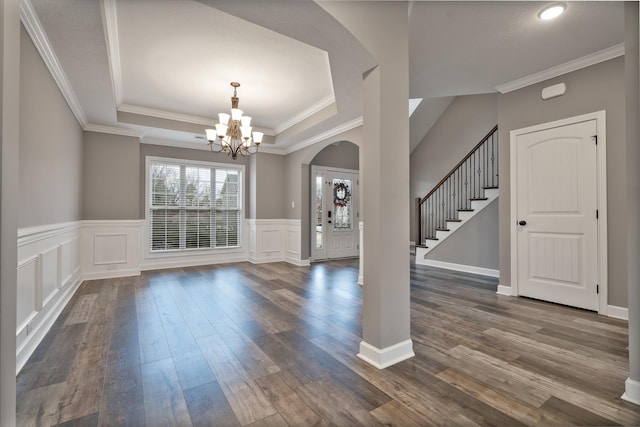 entryway with a raised ceiling, dark wood-type flooring, a chandelier, and ornamental molding