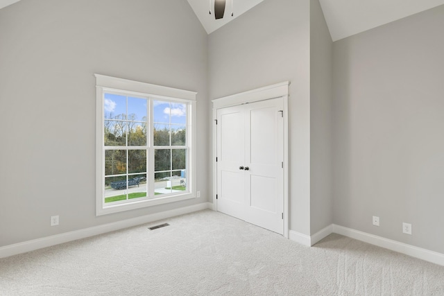 unfurnished bedroom with light carpet, a closet, high vaulted ceiling, and ceiling fan