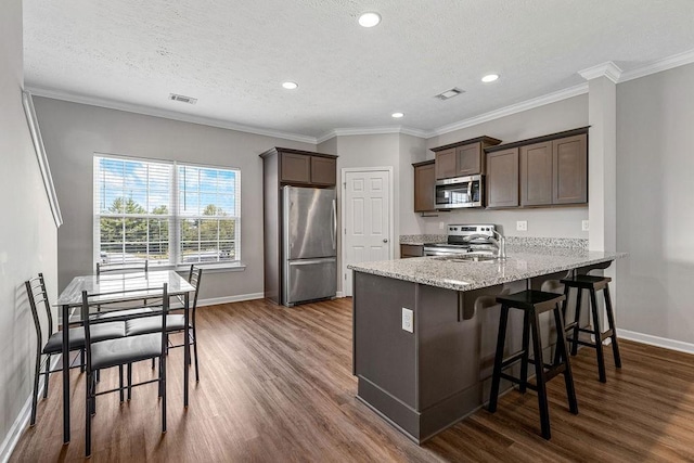 kitchen with dark brown cabinetry, dark hardwood / wood-style flooring, stainless steel appliances, and ornamental molding