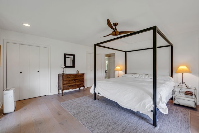 bedroom with light wood-type flooring, ceiling fan, and multiple closets