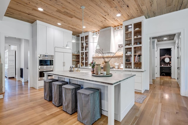 kitchen featuring pendant lighting, stainless steel double oven, a kitchen island with sink, and wood ceiling