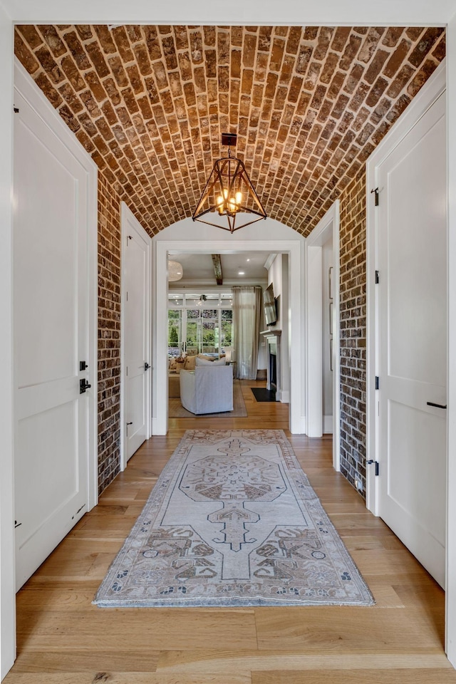 entrance foyer with light hardwood / wood-style flooring, vaulted ceiling, a notable chandelier, brick ceiling, and brick wall