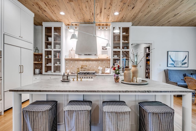 kitchen with pendant lighting, a breakfast bar, exhaust hood, white cabinets, and wood ceiling