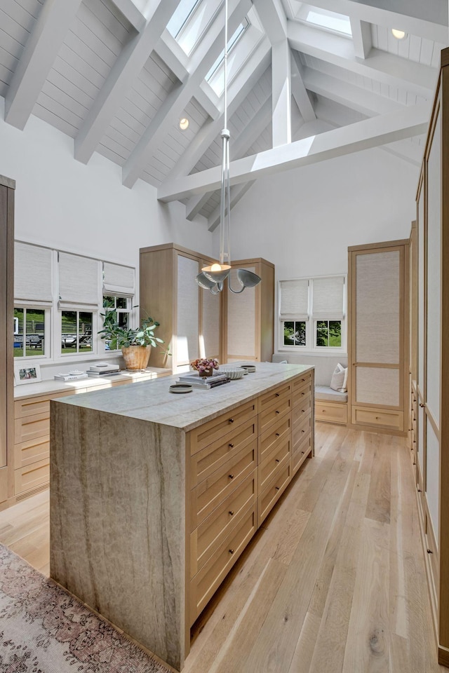 kitchen with a skylight, a large island, hanging light fixtures, high vaulted ceiling, and light hardwood / wood-style floors